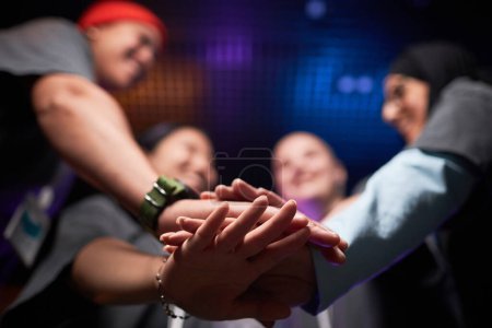 Photo for Low angle closeup of female team stacking hands in unity and celebrating victory on stage during competitive eSports event - Royalty Free Image