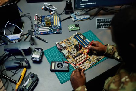 Hands of young African American repairman using electric tweezers to solder tiny details of microchip on motherboard