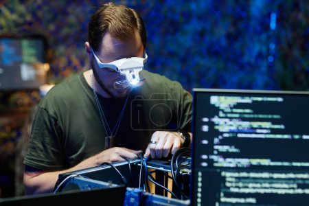 Foto de Joven ingeniero o técnico que usa gafas con cables de control de lámpara del procesador de computadora mientras se inclina sobre él por su lugar de trabajo - Imagen libre de derechos