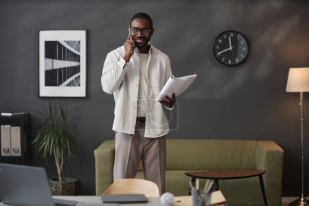 Téléchargez les photos : Portrait complet de l'entrepreneur afro-américain adulte parlant au téléphone pendant l'appel de travail dans l'intérieur du bureau moderne, espace de copie - en image libre de droit