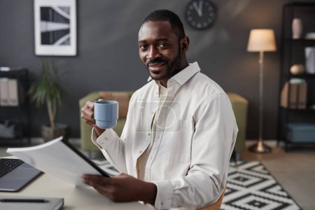 Photo for Portrait of smiling African American man looking at camera at home office and holding coffee cup, copy space - Royalty Free Image