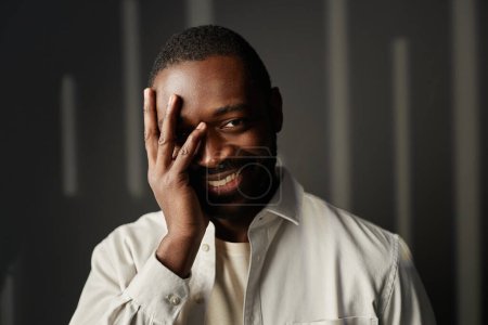 Photo for Front view portrait of carefree Black man smiling at camera with hand covering face - Royalty Free Image
