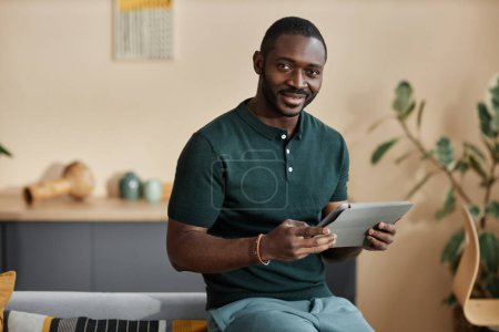 Photo for Waist up portrait of smiling African American man holding digital tablet and smiling at camera in home setting, copy space - Royalty Free Image