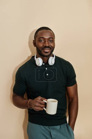Photo for Vertical portrait of handsome adult African American man standing against neutral background with cup of coffee - Royalty Free Image