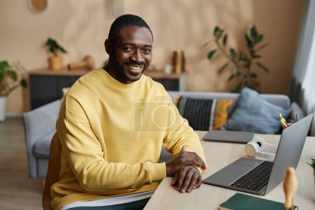 Portrait d'un homme noir adulte souriant regardant une caméra assise au bureau à la maison, espace de copie