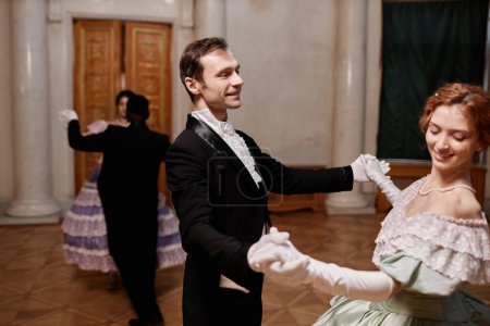 Portrait of smiling gentleman wearing classic tailcoat dancing with young lady during debutante ball in palace, copy space