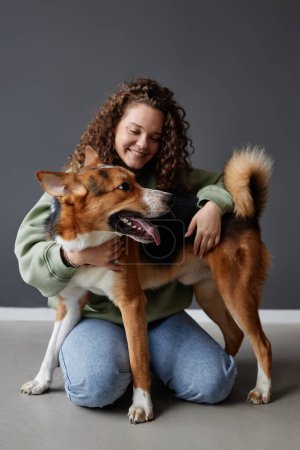 Full length portrait of happy young woman playing with mixed breed dog sitting on floor in studio