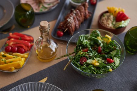 Cerrar imagen de fondo de la ensalada verde abundante en un tazón de vidrio con jarra de aceite de oliva en el espacio de copia de la mesa de la cena