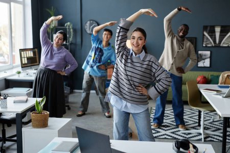 Foto de Diverso grupo de personas alegres disfrutando de ejercicios de estiramiento en la mañana comenzando la jornada laboral en la oficina - Imagen libre de derechos