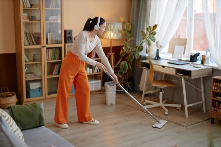 Ganztägiges Porträt einer jungen Frau, die Böden wischt und zu Hause Musik hört, während sie Kopierraum putzt