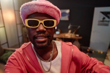Téléchargez les photos : Point de vue de l'homme afro-américain portant une tenue rose avec des lunettes de soleil enregistrement vidéo pour les médias sociaux à l'intérieur de l'espace de copie - en image libre de droit
