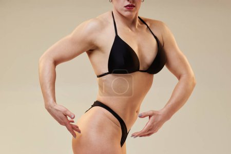 Cropped shot of unrecognizable female bodybuilder in quarter turns pose presenting her upper body physique isolated in studio on neutral background, copy space