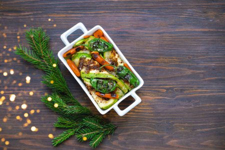 Gebackenes oder gegrilltes Gemüse in einer Keramikschale auf Holzuntergrund. Köstliches Essen zu Hause zubereiten. Kreativer Raum für Weihnachts- oder Neujahrsgestaltung. 