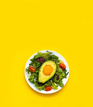 Baked egg with avocado and lettuce leaves on yellow background. Healthy and balanced products on a white plate. Fodmap diet ingredients. Close-up