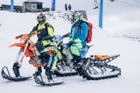 Téléchargez les photos : Two snowboarders sit on moto snowmobile on snow high in mountains - en image libre de droit