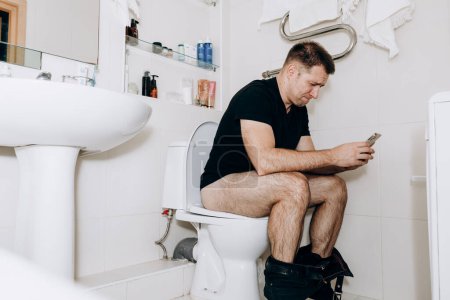 Photo for Man is sitting on toilet with phone in his hand. Guy's morning routine - Royalty Free Image