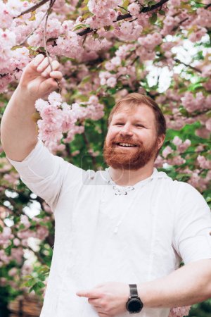 Porträt eines Mannes mit rotem Bart im blühenden Garten. Gleichstellung der Geschlechter. Der Frühling kam