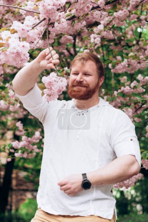 Portrait of man with red beard in blooming garden. Gender equality. Spring came
