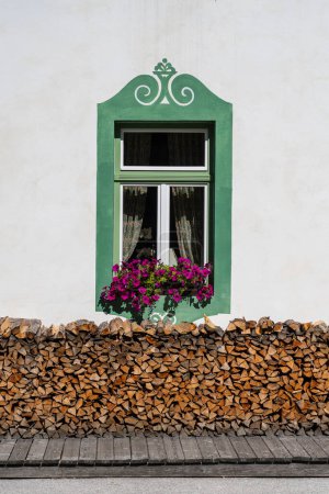 Photo for White facade of a old farm mountain house and windows with flowers and near the wall are a complex pile of firewood in the Dolomites, Italy, close up - Royalty Free Image