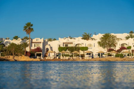 Photo for Buildings, sun loungers and parasols are reflected in the calm sea water on the beach in the resort town of Sharm El Sheikh during sunrise, Egypt - Royalty Free Image