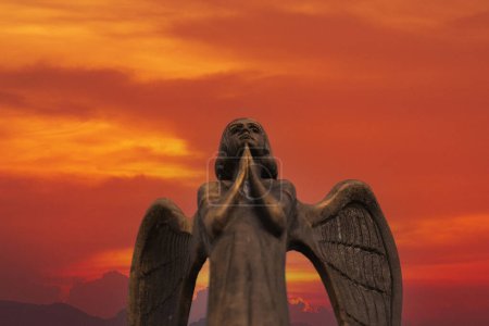 Téléchargez les photos : Détail de la belle statue en bronze d'un ange avec des ailes contre le ciel rouge. Bel ange avec un fond de ciel rouge avec espace pour le texte, gros plan - en image libre de droit