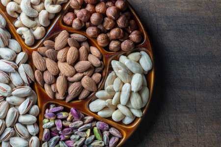 Photo for Assortment of nuts in ceramic bowl on a wooden background, close up, top view, copy space. Cashew, hazelnuts, pistachios and almonds nuts for eat. Vegetarian meal. Healthy eating concept - Royalty Free Image