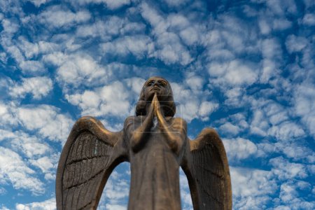 Téléchargez les photos : Détail d'une belle statue en bronze d'un ange avec des ailes contre le ciel avec des nuages blancs. Bel ange avec un fond bleu ciel avec espace pour le texte, gros plan - en image libre de droit