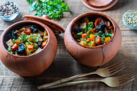 Photo for Stewed potato, carrot, onion, tomato and prunes in a clay pots with lid on wooden background, close up - Royalty Free Image