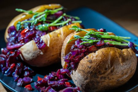 Foto de Patata rellena con col roja, tomate, pimientos y verduras en plato negro. De cerca. - Imagen libre de derechos