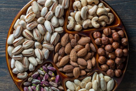 Photo for Assortment of nuts in ceramic bowl on a wooden background, close up, top view, copy space. Cashew, hazelnuts, pistachios and almonds nuts for eat. Vegetarian meal. Healthy eating concept - Royalty Free Image