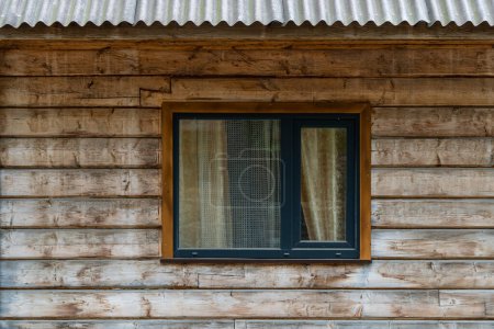 Foto de Una ventana en la fachada de madera de una casa rústica hecha de vigas de madera en un pueblo de los Cárpatos montañas, Ucrania occidental, Europa, de cerca - Imagen libre de derechos