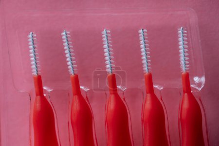 Photo for Red brushes for braces, toothbrushes for interdental spaces on pink background in plastic box, close up. Macro. The concept of good mouth hygiene - Royalty Free Image