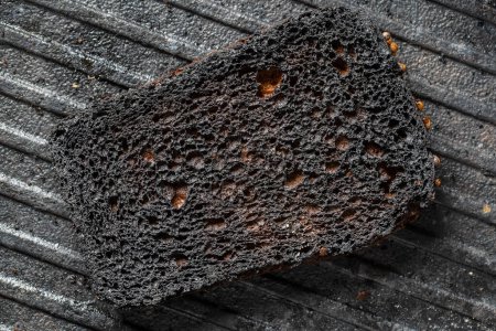 Foto de Burnt toast bread slice on a black cast-iron grill pan,, close up. Pattern of burnt black bread, abstract background, macro. Top view - Imagen libre de derechos