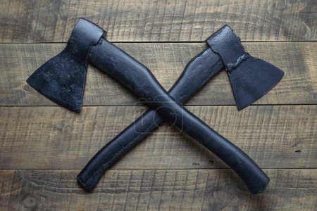 Foto de Two crossed black axes on wooden background, top view, close up - Imagen libre de derechos