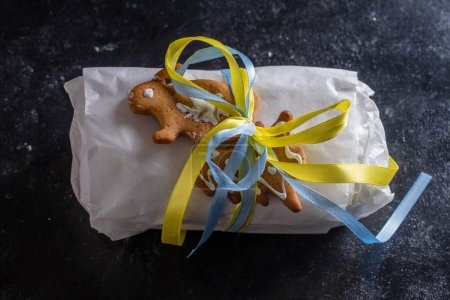 Photo for Christmas stollen wrapped in white paper with yellow and blue ribbon for a Christmas gift, traditional German bread for a festive pastry dessert. Close up - Royalty Free Image