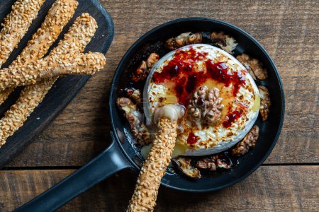Photo for View of baked on frying pan camembert cheese, walnuts, honey, jam and bread sticks with sesame seeds on wooden table background, close up, top view - Royalty Free Image