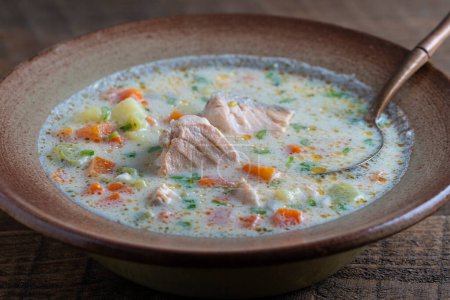 Téléchargez les photos : Fresh creamy salmon fish soup with potatoes, carrots, peppers and onions in a ceramic plate on a wooden table, close-up. A delicious dinner consists of fish soup with salmon - en image libre de droit