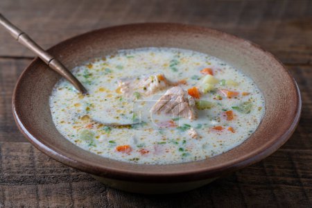 Fresh creamy salmon fish soup with potatoes, carrots, peppers and onions in a ceramic plate on a wooden table, close-up. A delicious dinner consists of fish soup with salmon