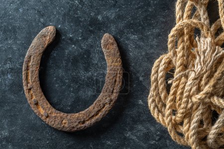 Foto de Old rusty horseshoe and rope on black background, close up, top view - Imagen libre de derechos