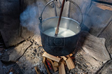 Foto de Making organic sheep cheese in wooden mountain Carpathian cheese factory with a boiling smoked cauldron with milk on open fire, Western Ukraine, Europe - Imagen libre de derechos