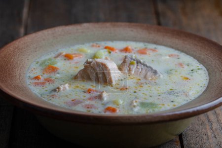 Téléchargez les photos : Soupe de poisson de saumon crémeux frais avec pommes de terre, carottes, poivrons et oignons dans une assiette en céramique sur une table en bois, gros plan. Un délicieux dîner se compose de soupe de poisson au saumon - en image libre de droit