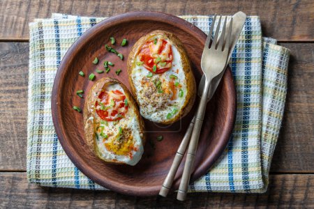 Foto de Baked potatoes stuffed with cheese, tomato, green onion and eggs in ceramic plate on wooden background, top view, close up - Imagen libre de derechos