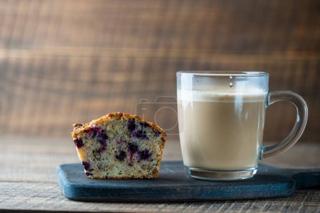 Foto de Delicious muffin with blueberries and cappuccino glass cup on a wooden table, close up. Fresh cupcake and coffee for breakfast - Imagen libre de derechos
