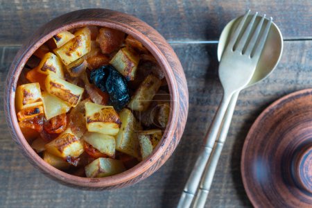 Photo for Stewed potato, carrot, onion, tomato and prunes in a clay pot on wooden table background, close up, top view - Royalty Free Image