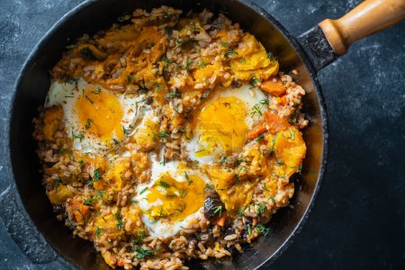 Photo for Boiled rice with fried eggs, pumpkin, peppers, carrots and onions in a cast iron pan, close up. Food background. Healthy food - Royalty Free Image