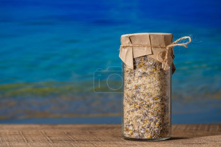 Téléchargez les photos : Sel himalayen de mer avec lavande sèche et fleurs de camomille dans un bocal en verre sur une table en bois avec le fond bleu de l'eau de mer par une journée d'été ensoleillée, gros plan, espace de copie - en image libre de droit