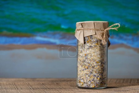 Téléchargez les photos : Sel himalayen de mer avec lavande sèche et fleurs de camomille dans un bocal en verre sur une table en bois avec le fond bleu de l'eau de mer par une journée d'été ensoleillée, gros plan, espace de copie - en image libre de droit