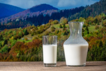 Téléchargez les photos : Du lait blanc frais dans une cruche et du verre sur une table en bois avec le fond des montagnes des Carpates d'automne, à proximité. Concept de produits laitiers - en image libre de droit