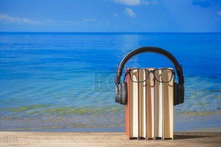 Foto de Conjunto de libros, auriculares y anteojos en mesa de madera cerca de agua de mar en la playa, de cerca. Audiolibros y concepto educativo - Imagen libre de derechos