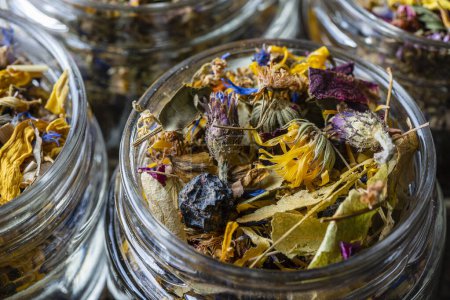 Téléchargez les photos : Dry flower and herbal tea leaves in a glass jar on wooden background, copy space. Herbal collection of chamomile, cornflower, mint, sea buckthorn, lemongrass, wild rose, dried citrus fruits and apple - en image libre de droit